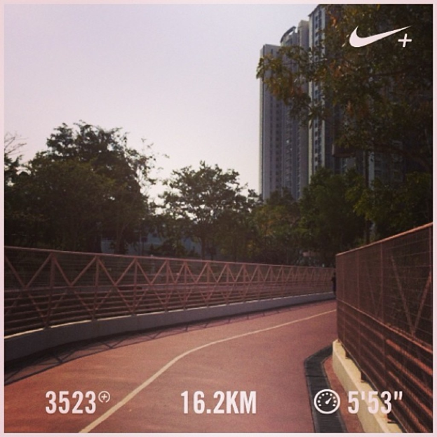 Eine Straße mit einem Zaun, Bäumen, einem Gebäude und einem Himmel, mit einem Wasserzeichen unten.