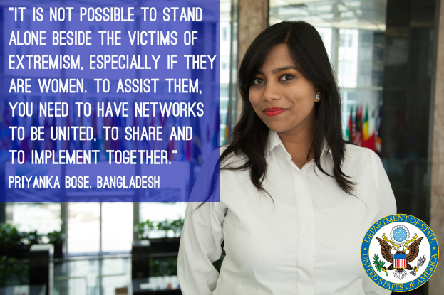 Eine Frau in einem weißen Hemd steht vor einem Gebäude mit einem Zitat über Einheit und Unterstützung für Opfer von Extremismus, insbesondere Frauen, mit einem Logo in der rechten unteren Ecke.