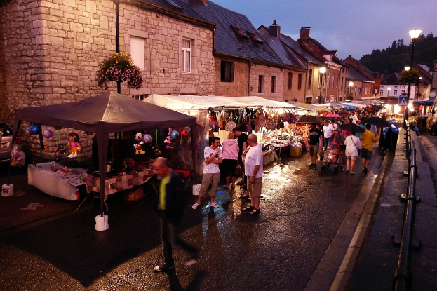 Eine Gruppe von Menschen, die auf einer Straße mit Geschäften, Bäumen und Straßenlaternen spazieren gehen, einige halten Schirme, mit Spielzeugen an den Geschäften und Barrikaden sichtbar.