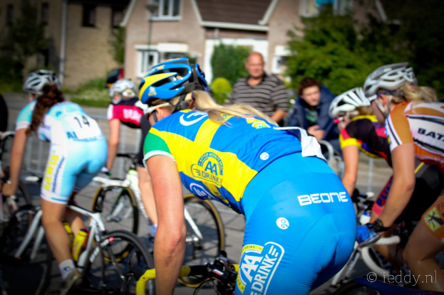 Mehrere Frauen auf Fahrrädern mit zwei Personen, die von oben zuschauen, Gebäude und Bäume im Hintergrund.