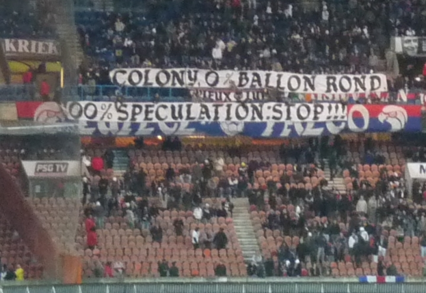 Ein Stadion voller Menschen, Banner und Stühle, mit einem Zaun unten und einer Treppe links.