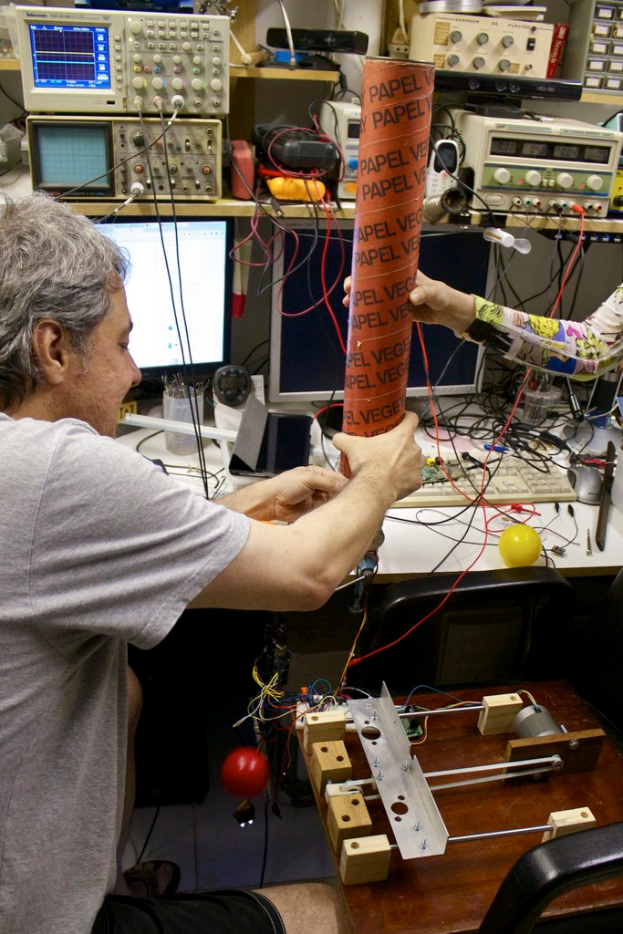 Ein Arbeitsplatz mit Maschinen, Kabeln, einem Computerdisplay, einem Kugelschreiberhalter, Menschen und einem Stressball.