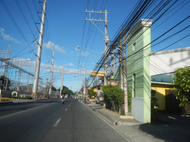 Stadtstraße mit Stromleitungen, Fahrzeugen, Gebäuden, Bäumen und Strommasten.