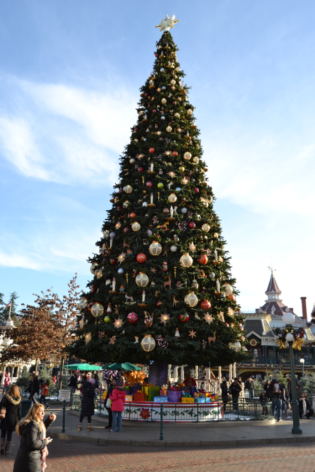 Ein dekorativer Weihnachtsbaum mit einem schwarzen Zaun vor zwei Mädchen, die sprechen, mit einem Schloss und trockenen Bäumen im Hintergrund.