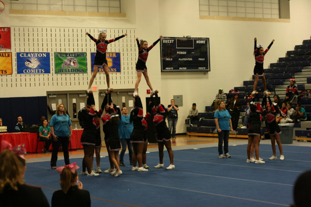 Menschen in verschiedenen Uniformen befinden sich auf einem Boden mit einer schwarzen Scorecard, Treppen und einem Tisch mit einer roten Decke.