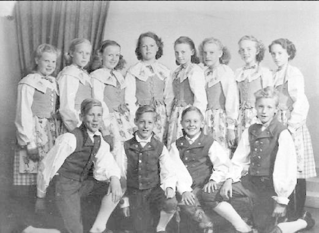 Schwarz-weiß-Foto von Kindern, die vor einer Vorhangwand posieren, mit dem Text "1930er-Kinder-Schule" unten.