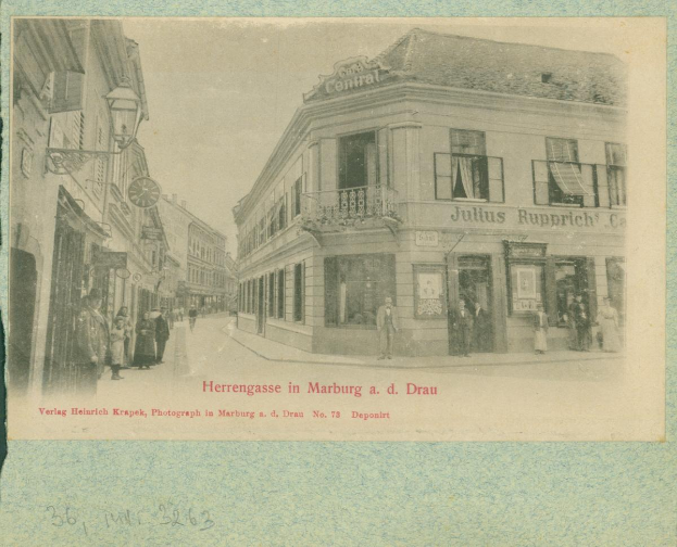 Ein altes Foto einer Straßenszene in Marburg, Deutschland, mit Gebäuden, Menschen und einem Himmel im Hintergrund, mit Text am unteren Rand des Bildes.