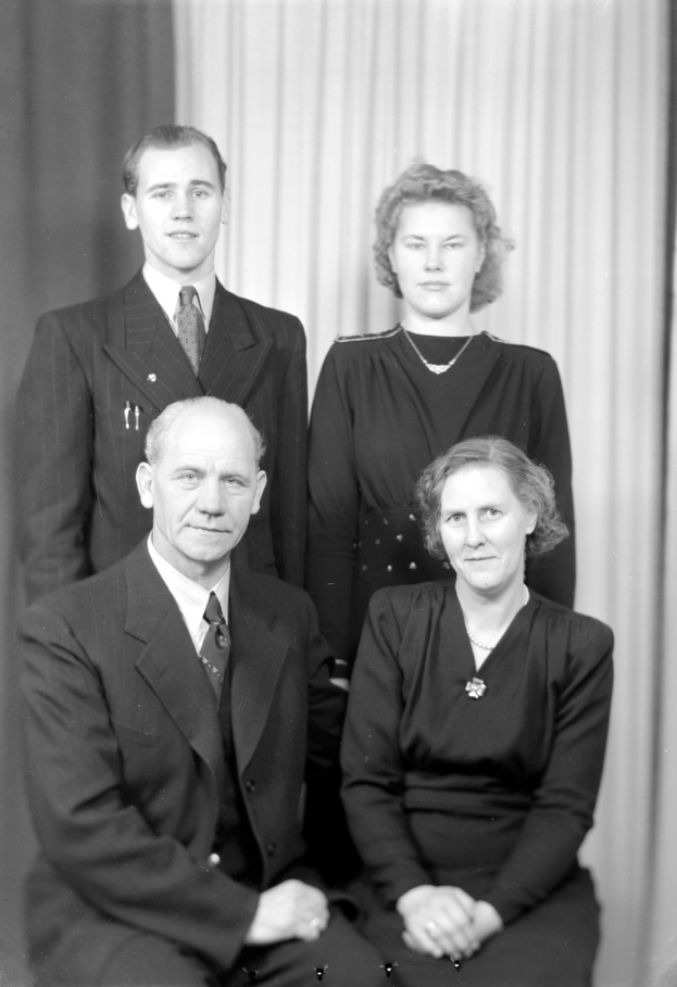 Ein Schwarz-Weiß-Foto von vier Personen, zwei Männern und zwei Frauen, alle in Anzügen, vor einem Vorhang.