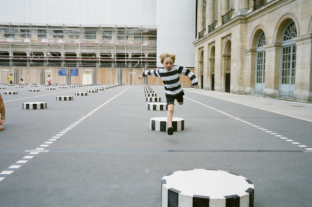 Vier Kinder befinden sich in einem Schulspielplatz mit schwarzen und weißen Betonstufen, ein Kind läuft auf dem Boden.