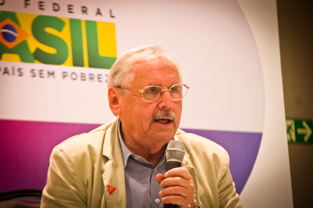 Eine Person, die in ein Mikrofon spricht und von einem Banner mit der Aufschrift 'Bundes' hinter ihr begleitet wird.