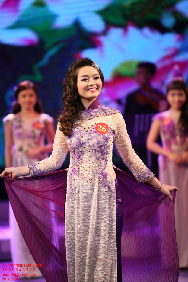 Eine Frau in einem cremefarbenen und violetten Kleid mit einem Anstecker darauf, mit einem unscharfen Hintergrund.