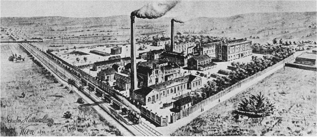 Ein altes Schwarz-Weiß-Luftbild der Wien, Illinois-Fabrik mit Rauch aus ihren Schornsteinen, umgeben von Gebäuden, Bäumen, Straßen, Fahrzeugen und Hügeln.