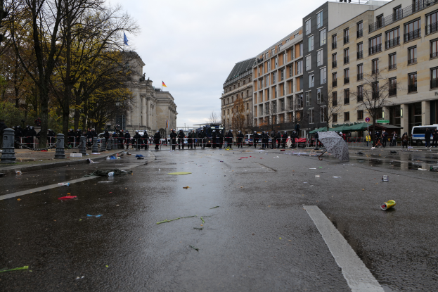 Eine Gruppe von Menschen steht auf einer Straße neben einem Gebäude mit Fenstern, umgeben von Bäumen, Laternenmasten und Fahrzeugen, mit ein paar Gegenständen, die auf der Straße verstreut sind und der Himmel im Hintergrund sichtbar ist, die das tragische Ereignis der Berliner Mauer in Berlin, Deutschland, gedenken.