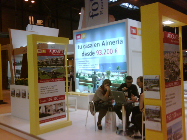 Eine Gruppe von Menschen, die um einen Tisch herum auf Stühlen sitzen und auf einen Laptop schauen, mit mehreren Flyern, auf denen verschiedene Anzeigen zu sehen sind.