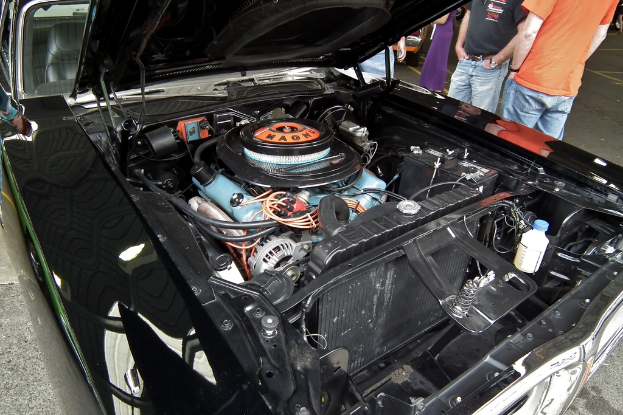 Nahaufnahme einer Autofrontpartie mit Menschen und Straße im Hintergrund.