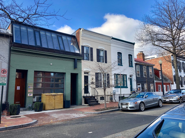 Eine Straße in einem Stadtteil von Philadelphia mit parkenden Autos, Gebäuden, Bäumen, Laternen, Schildern und Holzboxen unter einem bewölkten Himmel.