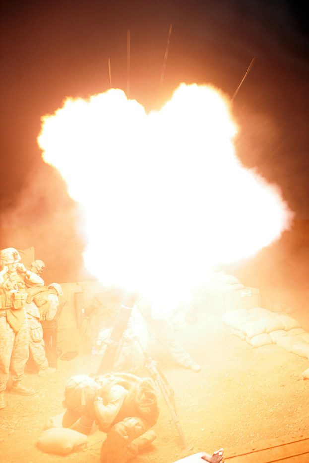 Mehrere Personen in Uniformen und Helmen befinden sich auf einem Gelände mit einigen Säcken, die herumliegen, und ein Feuer brennt in der Mitte der Szene.