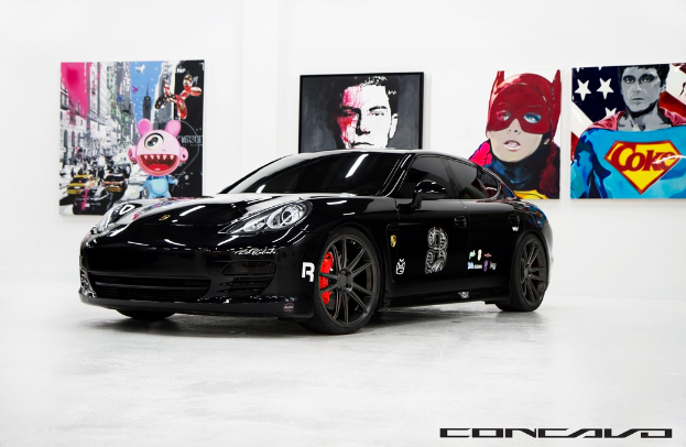 Ein schwarzer Nissan-Sportwagen parkt vor Cartoon-Postern, mit einer kleinen Inschrift am unteren Bildrand.