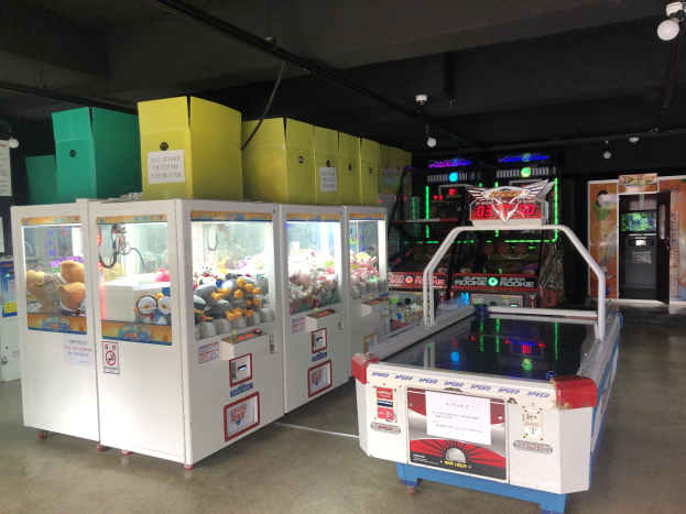 Ein Raum voller verschiedener Arcade-Spiele, mit einem Spielautomaten auf der rechten Seite, einem sichtbaren Boden und Deckenlampen.