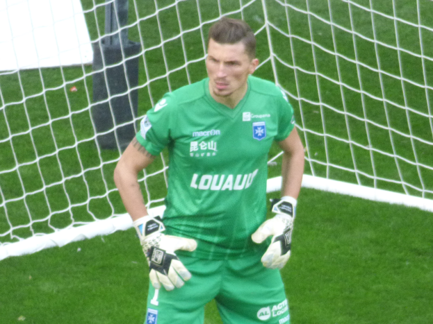 Ein Torwart in grüner Uniform steht vor einem Fußballtor, trägt Handschuhe auf einem Rasenfeld.