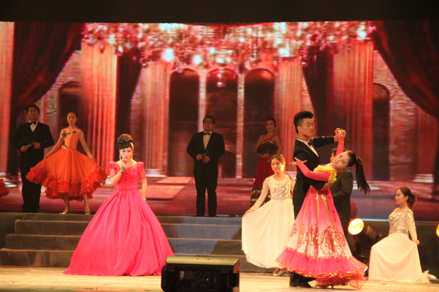 Eine Gruppe von Menschen auf einer Bühne mit Lichtern, Stufen und einem Hintergrundbild, mit einem Lautsprecher unten, was auf eine Tanzvorstellung hinweist.