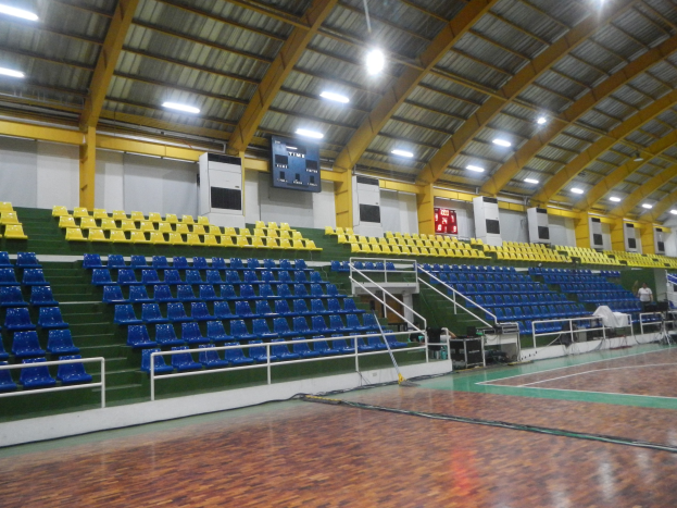 Große Halle mit Holzboden, blauen und gelben Sitzplätzen, Geländern, Treppen, Wandbildschirmen, Deckenleuchten und einigen Personen.