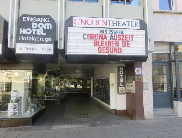 Außenansicht des Lincoln Theaters in Berlin, Deutschland, mit Glasfenstern und -türen sowie einer Tafel mit Text und einem belebten Innenraum.