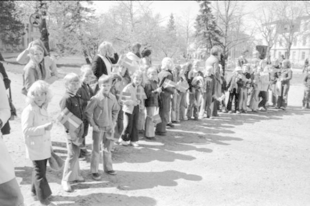 Eine Gruppe von Menschen steht in einer Reihe auf einem Schotterweg, hält Fahnen, mit Bäumen, Gebäuden und einem klaren Himmel im Hintergrund, auf einem Schwarz-Weiß-Bild einer Protestdemo auf dem Schulgelände.