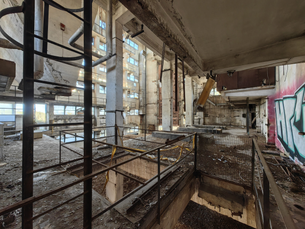 Verlassener Gebäuderaum mit Graffiti an den Wänden, bröckelnden Strukturen, Geländern, Pfählen, Rohren und zerbrochenen Fenstern, mit einem Wasserzeichen unten.