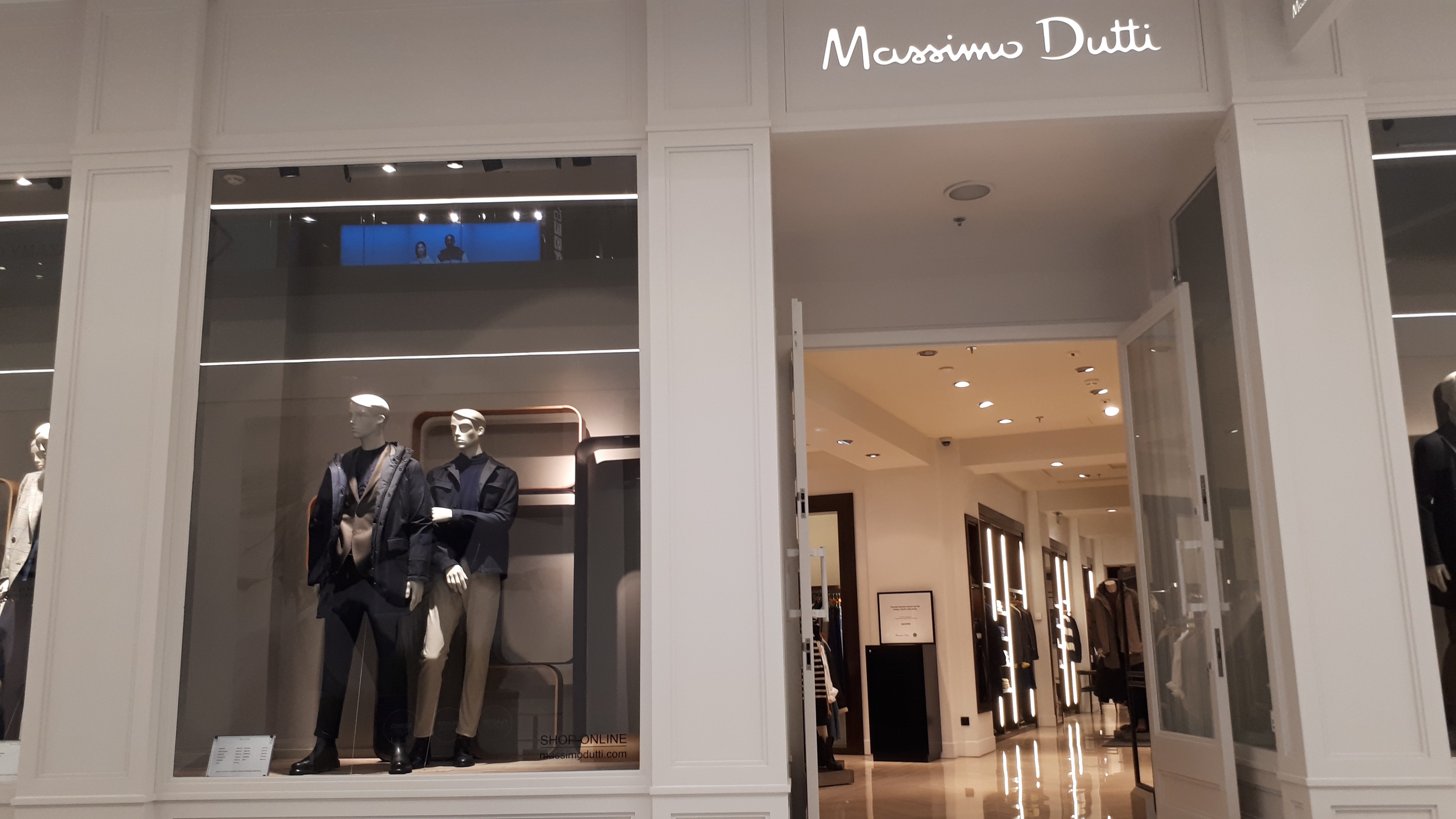 Innenansicht des Massimo Dutti Geschäfts in Mailand, Italien, mit Schaufensterpuppen in aktueller Mode, beleuchteter Decke, Informationsschildern und sichtbarem Boden.