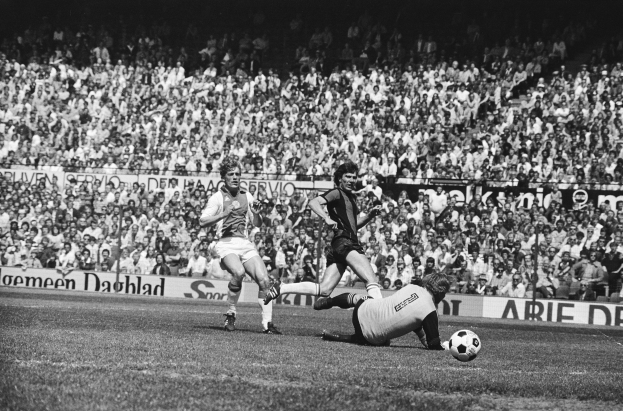 Schwarzes und weißes Foto von Fussballspielern im Einsatz auf einem Feld mit Zuschauern im Hintergrund und einer Bundesliga 1978-79 Ajax 1-1 Hannover 96-Banner.