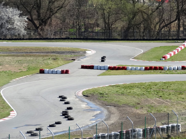 Rennstrecke mit zahlreichen Reifen entlang ihrer Kanten, umgeben von Gras und Maschendrahtzaun, mit Bäumen im Hintergrund.