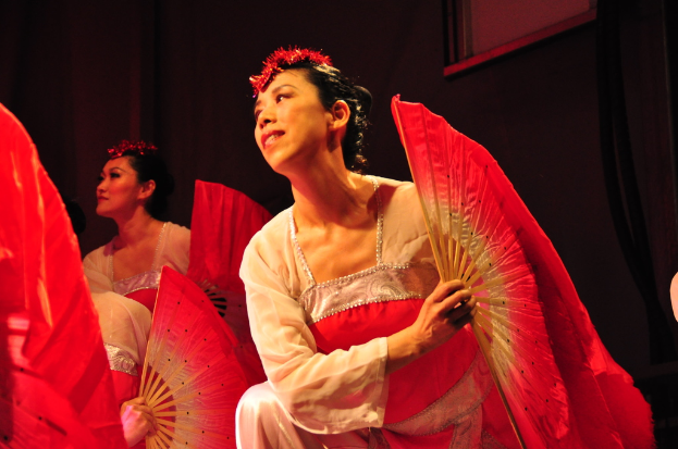 Eine Gruppe von Menschen, die Fächer in der Hand halten, mit einem gerahmten Bild im Hintergrund.