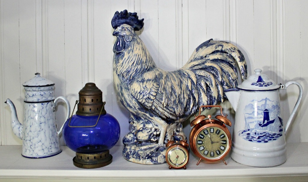 Eine Sammlung von Krügen, eine Laterne, Uhren und eine Hahnenskulptur auf einem Tisch.