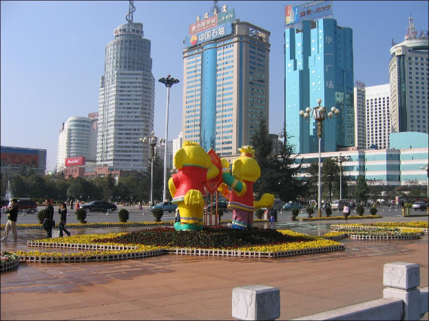 Eine Straßenszene mit Gebäuden, die Namensschilder an der Spitze, Laternenpfähle, einige Fußgänger, aufblasbare Spielbälle, kleine Pflanzen, Bäume, Büsche und Fahrzeuge auf der Straße zeigen.