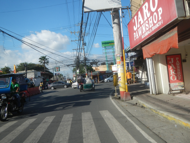 Eine belebte Stadtstraße mit Fahrzeugen, Fußgängern, Gebäuden und einem "Jaro Pfandleihhaus"-Schild auf der rechten Seite.
