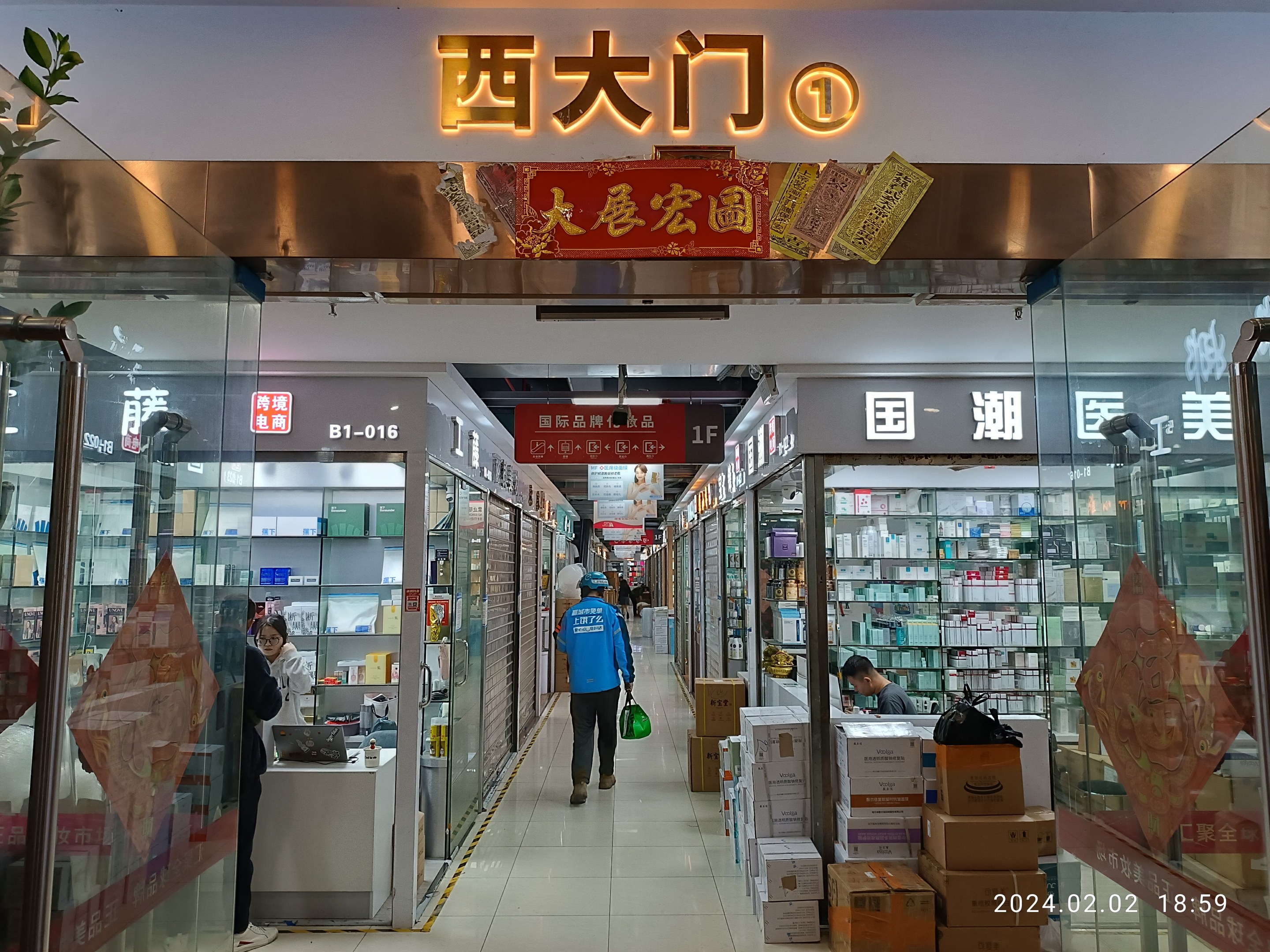 Innenansicht einer chinesischen Apotheke mit Glaswänden, Regalen voller Artikel, verstreuten Kartons auf dem Boden, einer Pflanze links und einem Namensschild oben.