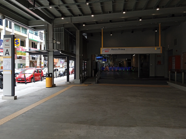 Leeres Parkhaus mit Autos zwischen Betonpfeilern, Deckenbeleuchtung, Informationsschildern an den Wänden und Gebäuden im Hintergrund.