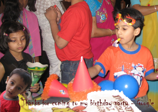 Kinder stehen vor einem Tisch mit einem Kuchen, Luftballons und Mützen, während andere Menschen im Hintergrund zu sehen sind.