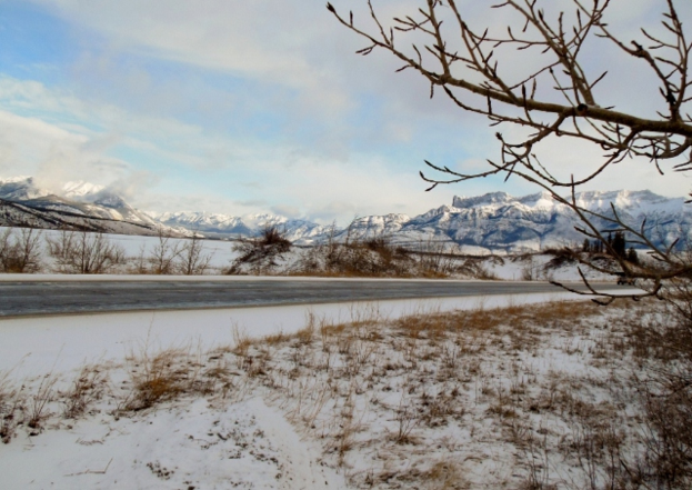 Eine Straße mit schneebedeckten Seiten und schneebedeckten Bergen im Hintergrund.