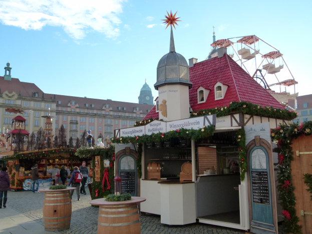 Ein geschäftiger Weihnachtsmarkt in Nürnberg, Deutschland mit Menschen um dekorierte Stände, festliche Lichter, ein Riesenrad im Hintergrund und eine Tafel mit Text auf der rechten Seite.