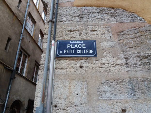 Ein Gebäude mit Fenstern, Rohren und einer Tafel mit der Aufschrift "Place du Petit College" an der Seite.