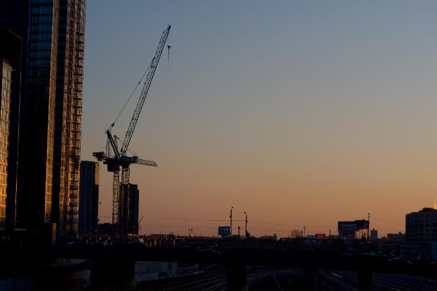 Gebäude auf der linken Seite, ein Kran, Strommasten und -leitungen, mit Himmel oben.