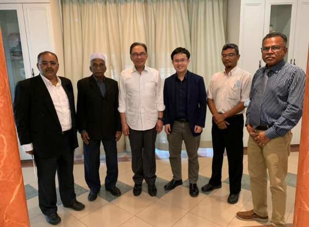 Eine Gruppe von Männern in einem formellen Raum mit zwei Säulen, Vorhängen und Schränken in Diskussion.