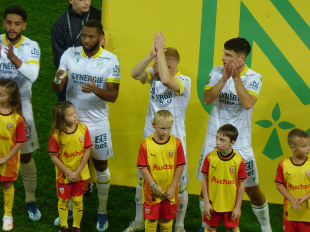 Eine Gruppe von Fußballspielern in Uniformen klatscht in celebration auf einem Ligue 1-Feld, mit einem "Ligue 1"-Schild im Hintergrund.