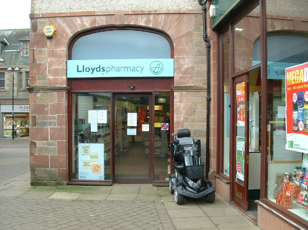 Eine Apotheke mit einem Fahrzeug davor und einem Geb├Ąude in der linken Ecke.