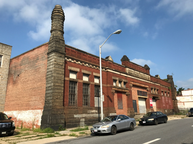 Außenansicht einer ehemaligen Feuerwache in St. Louis, ein altes Backsteingebäude mit einem Seitenkamin, umgeben von Straßeninfrastruktur einschließlich Pfosten, Laternen, Fahrzeugen, Schildern und Bäumen unter einem bewölkten Himmel.