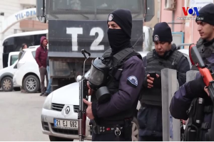 Eine Gruppe von Polizisten in Uniformen, die Waffen halten, steht auf einer Straße in Ankara, Türkei, während einer Anti-Regierungsdemo, mit Fahrzeugen, Menschen, Gebäuden und Texttafeln im Hintergrund.