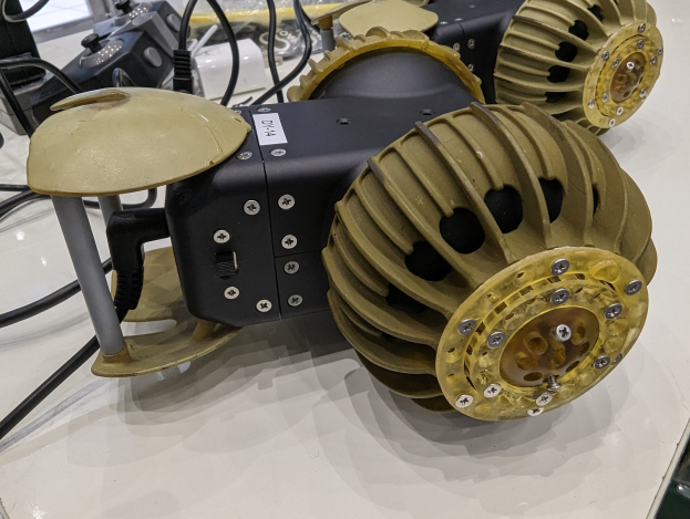 Nahaufnahme eines schlanken, metallischen 3D-gedruckten Roboters mit detaillierten Elementen auf einem Tisch umgeben von Kabeln.