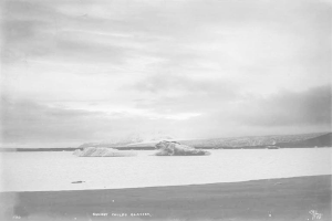 Ein Schwarz-Wei├č-Foto eines Eisbergs, der im Ozean treibt, umgeben von H├Ąngen und einer bew├Âlkten Himmel, mit dem Text "Sunset Childs Glacier" unten.